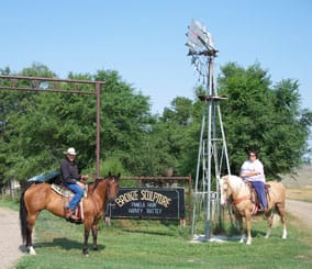 Harvey and his daughter horseback at the gate to their home and gallery near Glendive, Montana.
