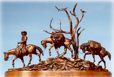 Bronze sculpture of a cowboy with his horse and his two pack horses.