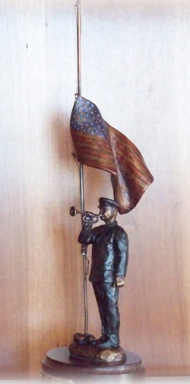 Bronze sculpture of soldier playing taps with half-mast American flag.
