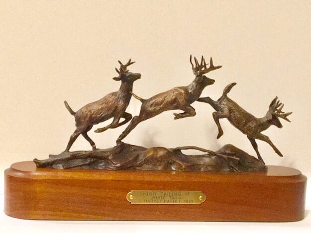 Bronze sculpture of three whitetail bucks running.