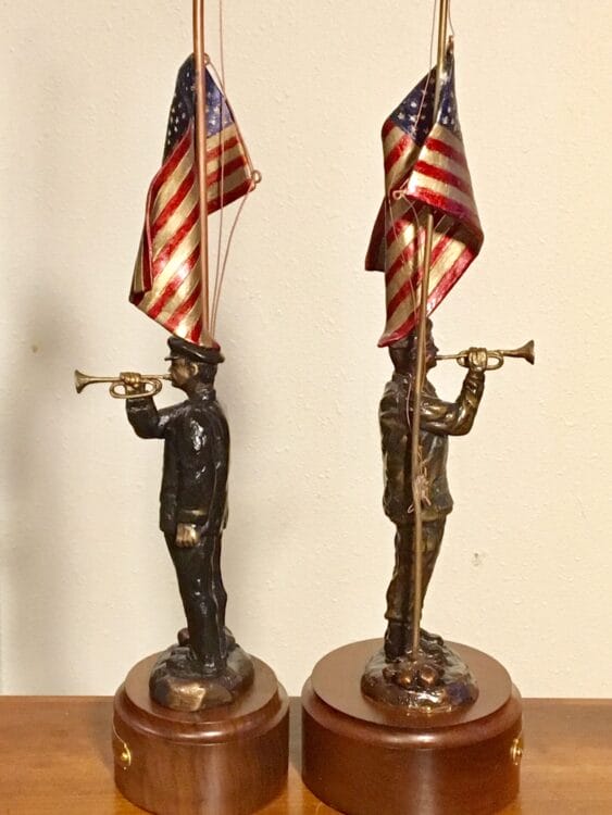 Side view of two sculptures of an American soldiers playing taps beside an American flag.