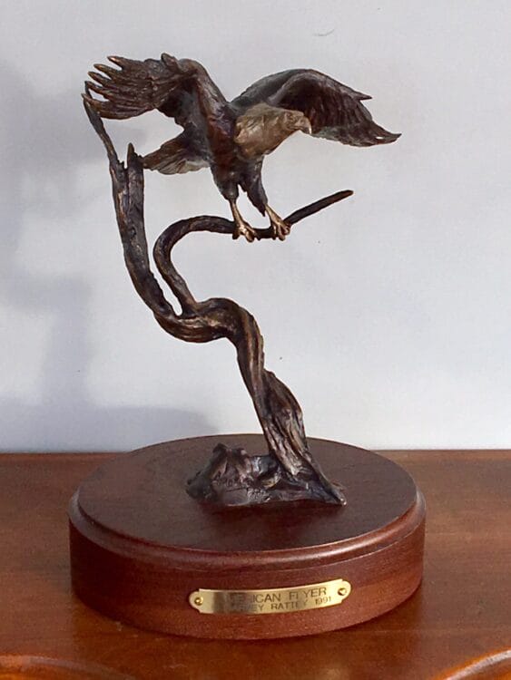 A bronze sculpture of a bald eagle landing on a tree.