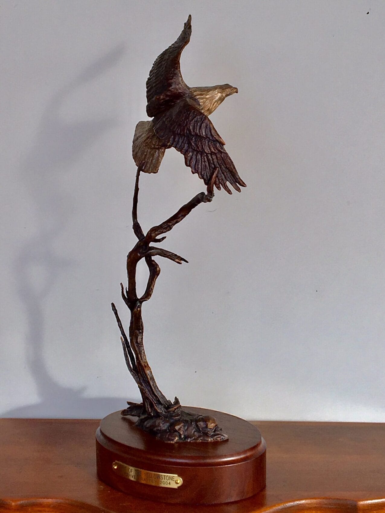 Bronze sculpture of a bald eagle lifting off from a tree.